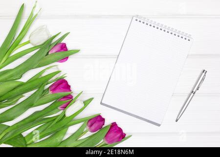 Ouvrez le carnet vierge, stylo avec fleurs de tulipe. Vue de dessus, plan d'appartement. Concept féminin abstrait. Arrière-plan de la maquette de printemps Banque D'Images