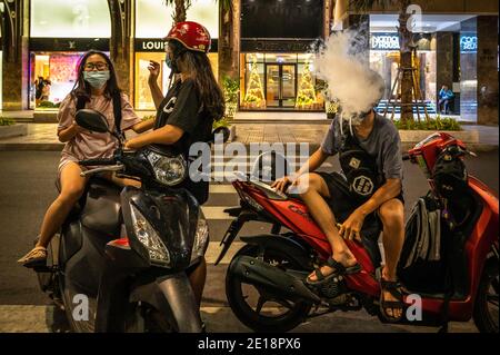 Un jeune homme qui fume pendant que deux filles parlent tout en traînant dans le centre de Ho Chi Minh ville, Vietnam Banque D'Images