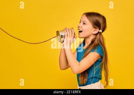 Une adolescente positive dit dans une boîte peut téléphone, jouant dans le chat rétro connecté, sur fond jaune. Concept de câbles croisés et conversation téléphonique Banque D'Images