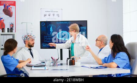 Femme sénior neurologue analysant les fonctions cérébrales à l'aide de la haute technologie dans la salle de conférence médicale, médecin testant de nouvelles innovations. Medic étudiant le diagnostic pour le traitement des patients travaillant dans la salle de réunion Banque D'Images