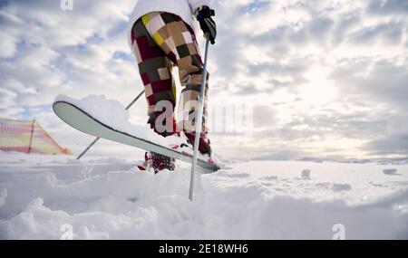 Gros plan, vue en angle bas des jambes du skieur. Homme ski, faire un saut sur une surface enneigée blanche contre un beau ciel nuageux. Copier l'espace. Concept des activités sportives d'hiver. Banque D'Images