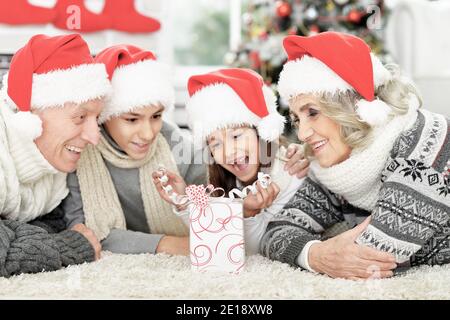 Bonne famille dans les chapeaux de père Noël sur le sol avec cadeau Banque D'Images