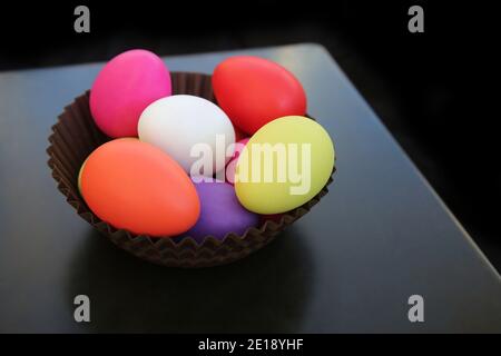 Œufs de pâques peints en plusieurs couleurs en rouge, rose, jaune, vert et blanc dans un panier en papier brun sur fond sombre. Banque D'Images