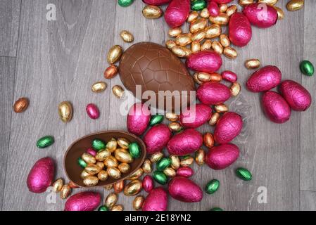 Pile ou groupe de plusieurs couleurs et différentes tailles d'oeufs de pâques au chocolat enveloppés de papier d'aluminium coloré dans le rose, le rouge, l'or et le vert. Grandes moitiés d'un bro Banque D'Images