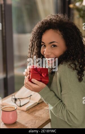 joyeuse femme afro-américaine tenant un cadeau de noël enveloppé dans un café Banque D'Images