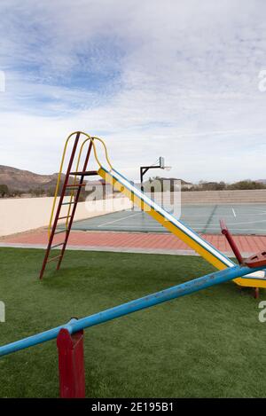 Un terrain de jeu vide dans le désert avec de l'herbe artificielle, un bac à thé, un toboggan et un terrain de basket-ball. Banque D'Images