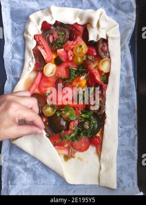 Une pizza préparée à la main humaine et faite maison avec des tomates fraîches et quelques feuilles de basilic. Banque D'Images