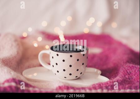 Tasse de café frais sur plateau sur chandail tricoté au-dessus des lumières brillantes gros plan. Bonjour. Heure du petit déjeuner. Banque D'Images