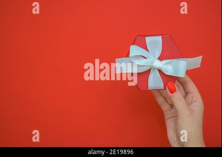 Les femmes tiennent une boîte cadeau rouge avec un ruban blanc sur un fond rouge avec un espace pour copier. Vue de dessus. Arrière-plan de la Saint-Valentin, arrière-plan de la fête des mères Banque D'Images