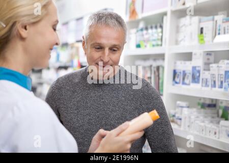 Homme principal et pharmacien professionnel examinant l'étiquette d'un produit médical. Jolie femme chimiste aidant son client masculin, lui offrant medicatio Banque D'Images