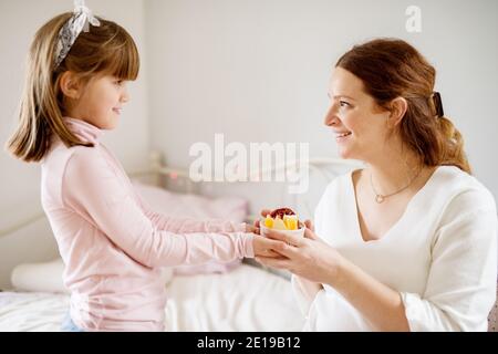 Adorable petite fille apportant une tasse avec salade de fruits à sa mère enceinte surprise. Concept de famille et de nouvelle vie. Banque D'Images