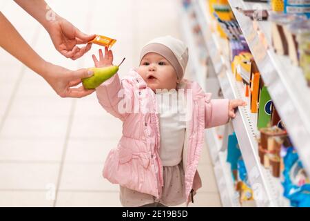 Shopping en famille. Un enfant mignon est debout près de l'étagère avec des produits, et choisira entre un bonbon et une poire, que la maman offre. Le concept de s. Banque D'Images