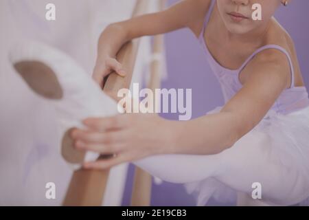 Petit gros plan d'une jeune ballerine qui s'étire avant de danser à l'école de ballet. Petite fille méconnaissable s'exerçant au studio de danse de ballet. Flexib Banque D'Images