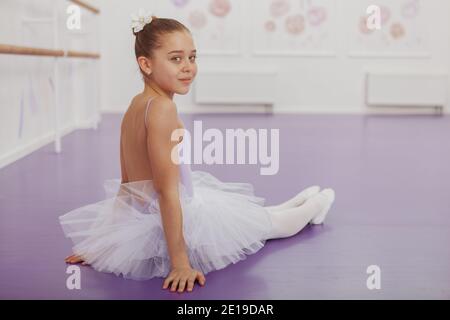 Vue arrière photo d'une belle ballerine gracieuse souriant à la caméra au-dessus de son épaule, assis sur le sol à la classe de ballet, espace de copie Banque D'Images