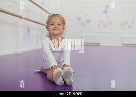 Bonne mignonne petite fille souriant à l'appareil photo, s'étirant avant la classe de ballet, l'espace de copie. Adorable petite ballerine s'exerçant avant la classe de ballet Banque D'Images