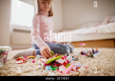 Petite fille floue jouant avec des blocs de jouets en plastique sur la moquette dans sa chambre. Banque D'Images