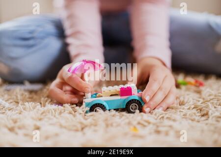 Voiture de jouet en plastique des blocs et parapluie sur le tapis en foyer devant la petite fille de prendre avec les mains. Banque D'Images