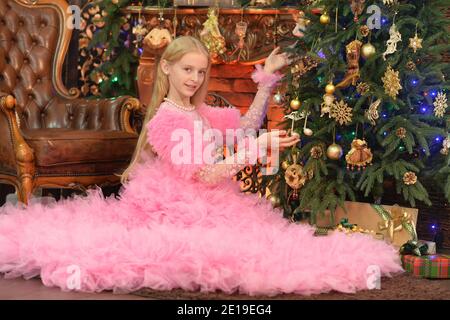 Belle fille en robe rose décorant arbre de Noël à la maison Banque D'Images