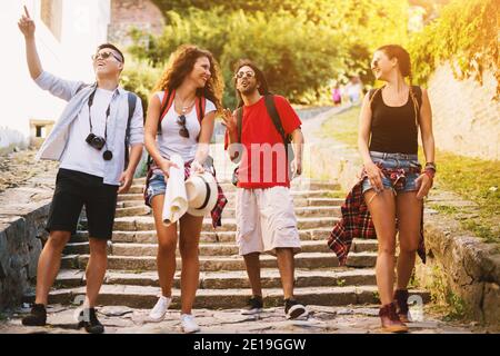 Quatre jeunes gens joyeux qui descendent les grands escaliers rocheux lors de vacances dans une vieille ville. Banque D'Images