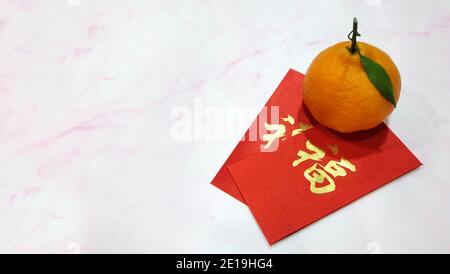 Un orange mandarin avec un ang pow rouge (un cadeau monétaire offert lors d'occasions spéciales dans la culture chinoise, en particulier le nouvel an chinois). Banque D'Images