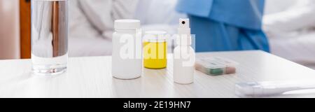 verre d'eau, récipients avec médicaments, spray pour la gorge et thermomètre sur table à l'hôpital, bannière Banque D'Images