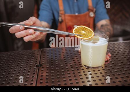 Gros plan sur un délicieux barman à cocktail mettant une tranche d'ornge sur. Un barman professionnel qui garante une boisson Banque D'Images