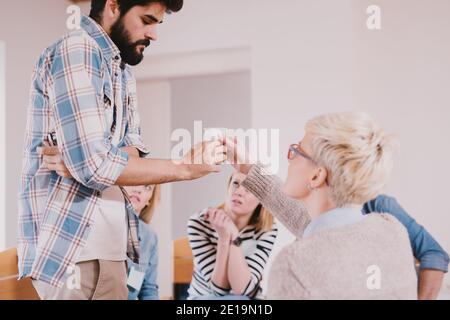 Les jeunes toxicomanes ayant une situation stressée tout en étant assis ensemble sur une thérapie de groupe spéciale. Contrarié barbu gars prenant de l'eau pour se calmer après lui Banque D'Images