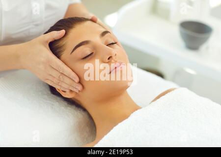 Mains du cosmétologue touchant la tête et vérifiant la peau ou la fabrication massage du visage pour la jeune femme Banque D'Images