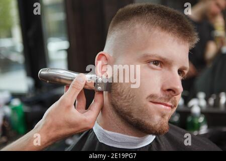 Gros plan sur un homme charmant souriant en train d'obtenir sa barbe taillée par barber Banque D'Images