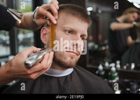 Client masculin au salon de coiffure, qui a taillé la barbe par un barbier professionnel Banque D'Images