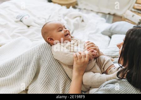 Jeune mère s'amuser avec un bébé garçon mignon au lit, tons naturels, amour émotion Banque D'Images