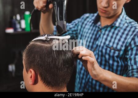 Coupe courte d'un homme méconnaissable qui se fait sécher les cheveux par un barbier professionnel. Le coiffeur d'un jeune homme souffle sécher les cheveux d'un client d'un homme Banque D'Images