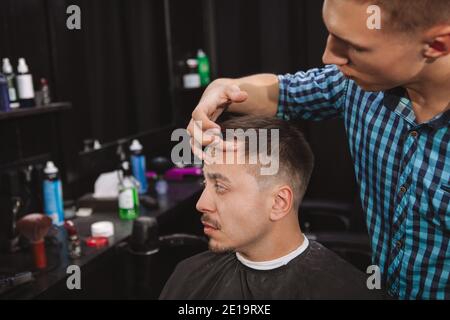 Photo courte d'un homme mûr regardant dans le miroir tout en coiffant ses cheveux. Coiffeur professionnel travaillant à la barbershop, coiffant de Banque D'Images