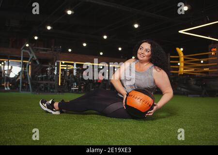 Bonne maturité femme de taille plus s'exerçant avec medecine ball à la salle de gym. Gai belle femme en surpoids faisant de l'exercice abs au studio de sport Banque D'Images