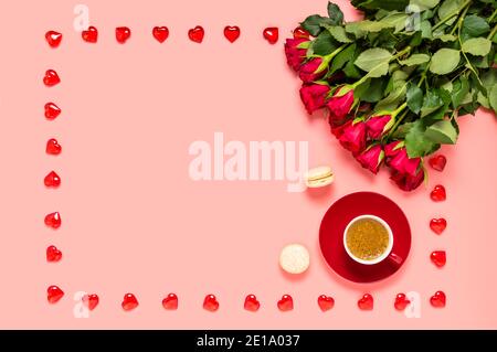 Bouquet de roses rouges, tasse de café et macarons avec cadre en coeurs de bois sur fond rose. Salutation de la fête des mères, des femmes ou de la Saint-Valentin. Amour Banque D'Images