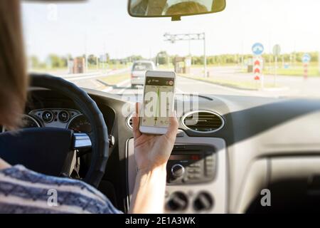 Femme pilote assis dans la voiture et tenant un smartphone mobile noir avec application de navigation gps cartographique avec itinéraire planifié à l'écran. Banque D'Images