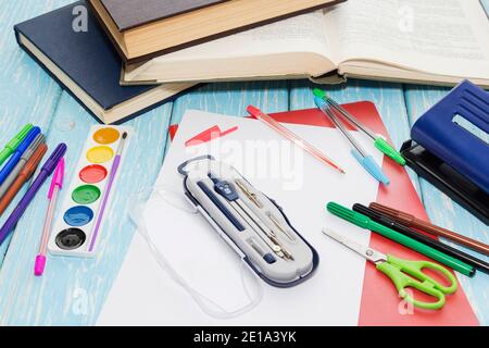 Fournitures scolaires sur fond bleu en bois, crayons, marqueurs, peintures, une feuille de papier. Banque D'Images