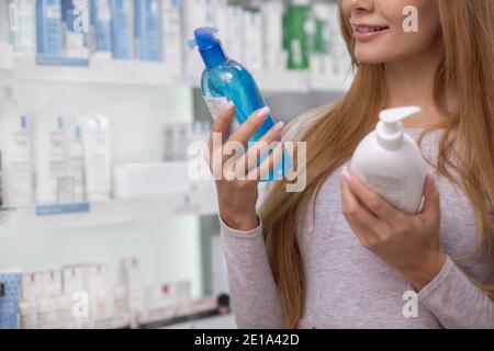 Prise de vue rognée d'une femme souriante, lecture d'une étiquette sur une bouteille de médicament, shopping en pharmacie. Une cliente examine les étiquettes des produits à la p Banque D'Images