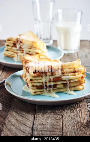 Crêpes fines, crêpes au lait condensé dans une assiette bleue sur une table en bois. Banque D'Images