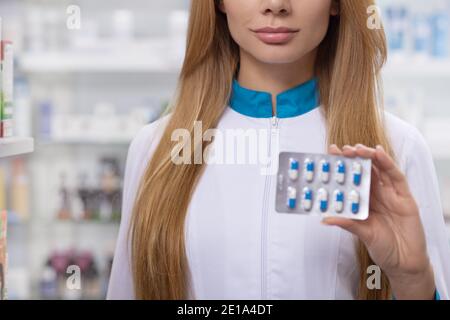 Courte vue rapprochée d'une pharmacienne tenant des comprimés blister à l'appareil photo, espace de copie. Chimiste professionnel vendant des produits médicaux au médicament Banque D'Images