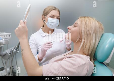 Une femme heureuse souriant regardant dans le miroir après un examen dentaire Banque D'Images