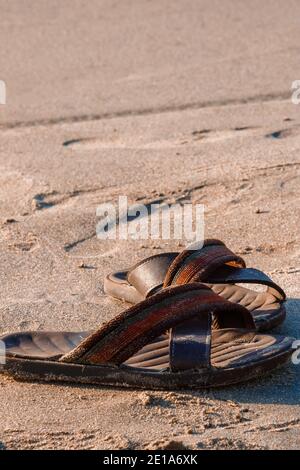 Une paire de sandales ou de tongs laissées par son propriétaire de voyageur sur la plage de sable tout en faisant un plongeon sur les eaux paisibles de la plage solitaire, c'est la kinf Banque D'Images