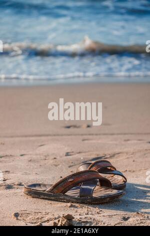 Une paire de sandales ou de tongs laissées par son propriétaire de voyageur sur la plage de sable tout en faisant un plongeon sur les eaux paisibles de la plage solitaire, c'est la kinf Banque D'Images
