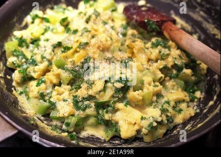 Œufs brouillés avec kale, oignons verts et céleri avec une saupoudrière de poivre de Cayenne dans une poêle avec une cuillère en bois. Banque D'Images
