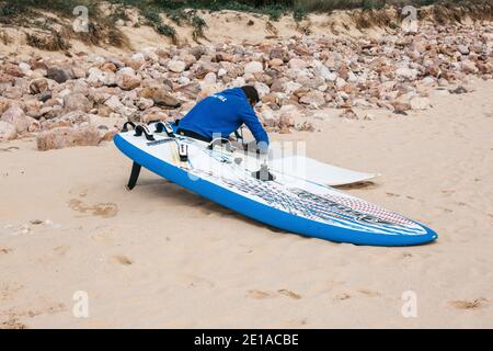 Portugal, Sintra, 29 mai 2019 : le surfeur répare une planche de surf sur la plage. Banque D'Images