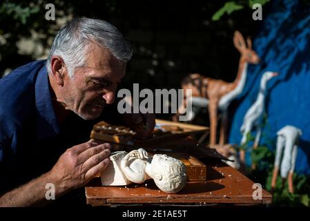 Un sculpteur Rufet Hanahmeydov travaille sur sa nouvelle création dans le village d'Anig, district de Qusar, Azerbaïdjan. Il a été la sculpture et la peinture de bois pendant près de 45 ans. Rufet dit qu'il prend toutes les idées de ses rêves. Maintenant Rufet sculpte un garçon tenant sa main et pleurant parce qu'il a été mordu par une guêpe. Banque D'Images