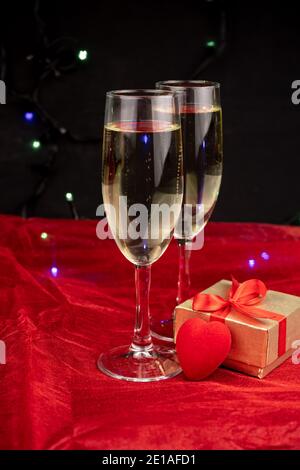 Deux verres avec champagne, boîte cadeau or et décor romantique sur fond noir et rouge Banque D'Images