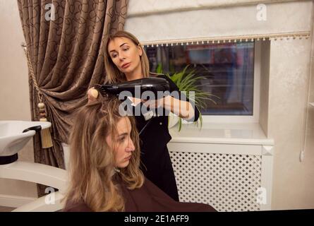 Coiffeur blond sécher les cheveux blonds du client avec un sèche-cheveux. Banque D'Images