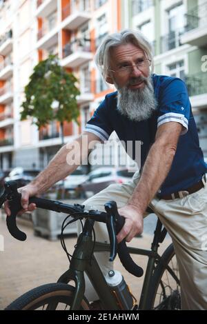 Prise de vue verticale en petit angle d'une barbe grise élégante homme en vélo dans les rues de la ville Banque D'Images