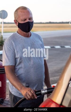 homme dans un masque de protection noir ravitailler une voiture à une station-service, protection contre les virus Banque D'Images